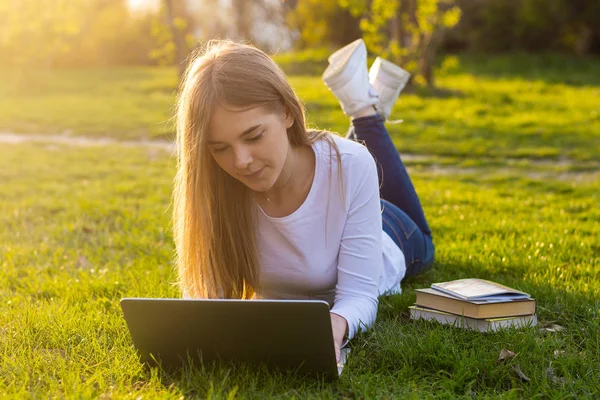 Joven hermosa mujer con un ordenador portátil se encuentra en la hierba en primavera —  Fotos de Stock