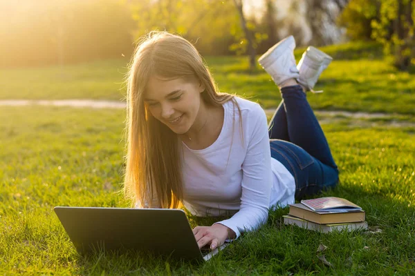 Joven hermosa mujer estudiante con un portátil se encuentra en la hierba en —  Fotos de Stock