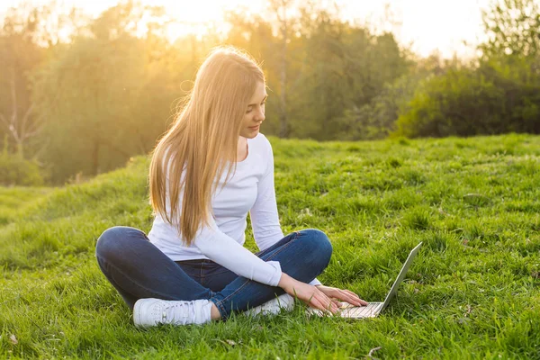 Mujer hermosa joven con un ordenador portátil sentado en la hierba en primavera un —  Fotos de Stock