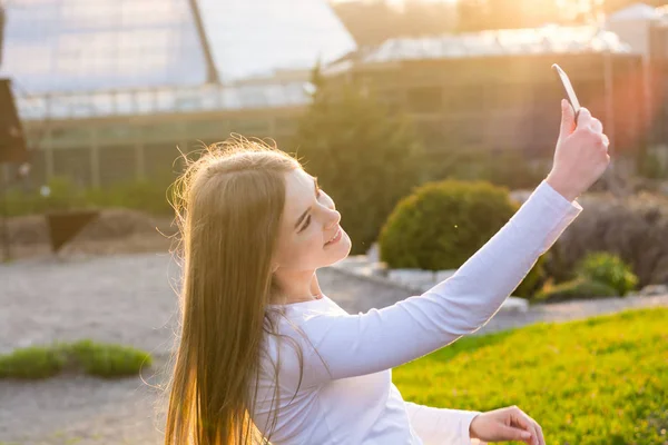 Uma jovem estudante rir e fazer selfie em um parque ao pôr-do-sol — Fotografia de Stock