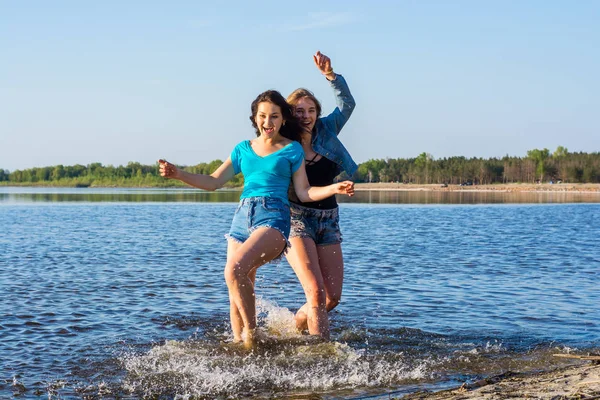 Los amigos están bailando y salpicando agua en la orilla del mar, riendo . —  Fotos de Stock