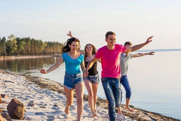 Amigos estão correndo ao longo da praia, de mãos dadas e risos — Fotografia de Stock