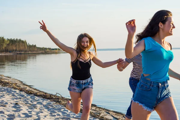 Друзья бегут по берегу моря, держатся за руки и смеются. — стоковое фото