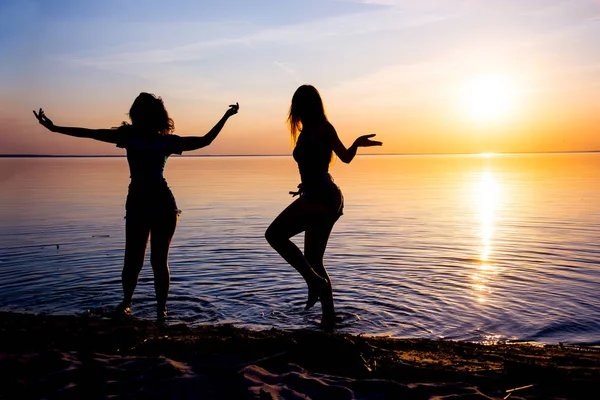 Dos chicas hermosas, estudiantes están bailando en la playa al atardecer —  Fotos de Stock