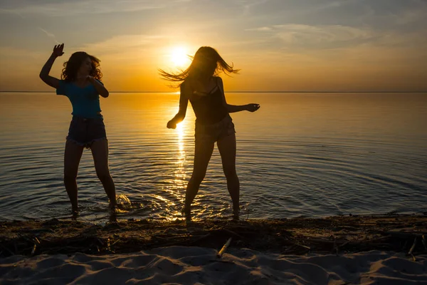 Dos chicas hermosas, estudiantes están bailando en la playa al atardecer —  Fotos de Stock