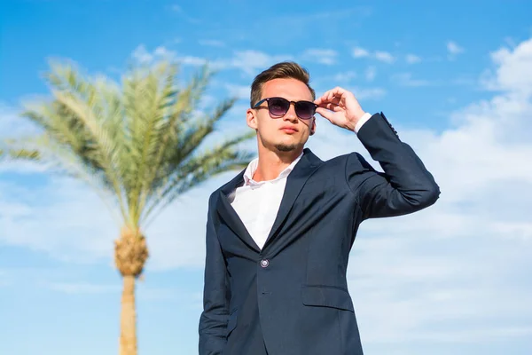 Young handsome man in a suit and white pants at the sea background  and palm trees. Fashion Model
