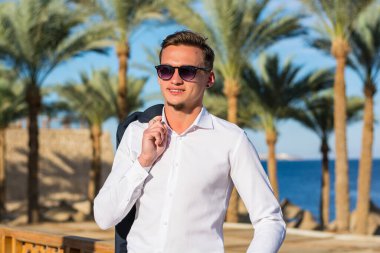 Palmiye ağaçlarında beyaz gömlekli genç ve yakışıklı bir adam ve kumsalda deniz altyapısı.. 