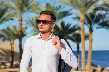 Palmiye ağaçlarında beyaz gömlekli genç ve yakışıklı bir adam ve kumsalda deniz altyapısı..