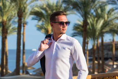 Palmiye ağaçlarında beyaz gömlekli genç ve yakışıklı bir adam ve kumsalda deniz altyapısı.. 