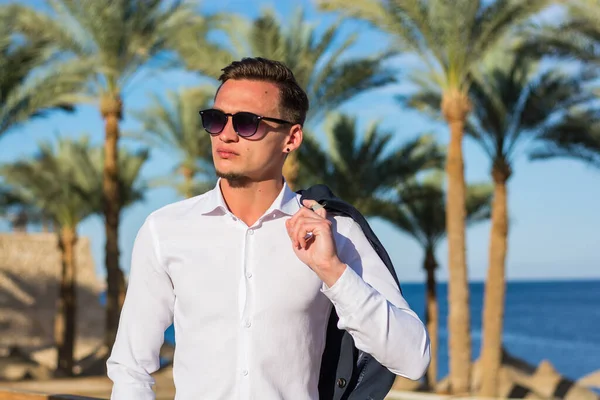 Palmiye ağaçlarında beyaz gömlekli genç ve yakışıklı bir adam ve kumsalda deniz altyapısı..