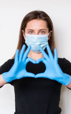 Young woman in medical mask and gloves shows a heart sign by hands. Quarantine clipart