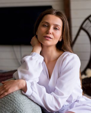 Beyaz kısa elbiseli güzel bir kadın evdeki hasır sandalyede oturuyor. Evde kal.