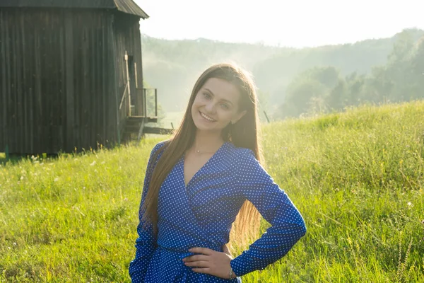 美しい若い女性は夏に古い工場の背景に野の花を持つ牧草地で太陽の下で笑っています — ストック写真
