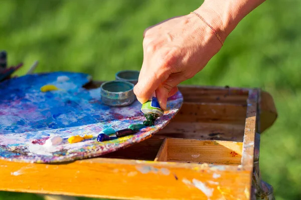 The artist's hand, which squeezes the oil paint from the tube into the palette on the easel, outdoor