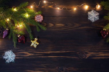 Şenlikli Noel arkaplanı, doğal ahşap masa yüzeyi ile çerçevelenmiş şablon ladin dalları, oyuncaklar ve yönlendirilmiş ışıklarla süslenmiş.