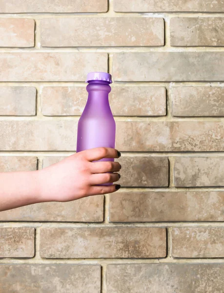 Βιολετί γυαλί ή πλαστικό μπουκάλι στο χέρι σε μπεζ φόντο — Φωτογραφία Αρχείου