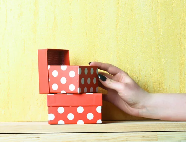 Caixa de presente manchado vermelho na mão feminina no fundo amarelo — Fotografia de Stock