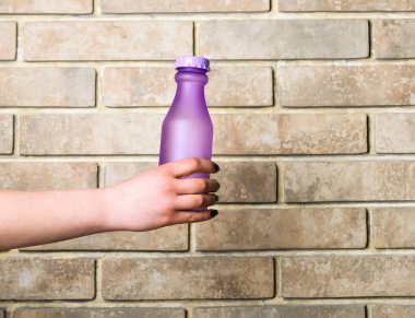 Menekşe cam veya plastik şişe bej renkli arka plan üzerinde elinde