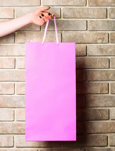 Saco de compras rosa na mão feminina na parede de tijolo — Fotografia de Stock