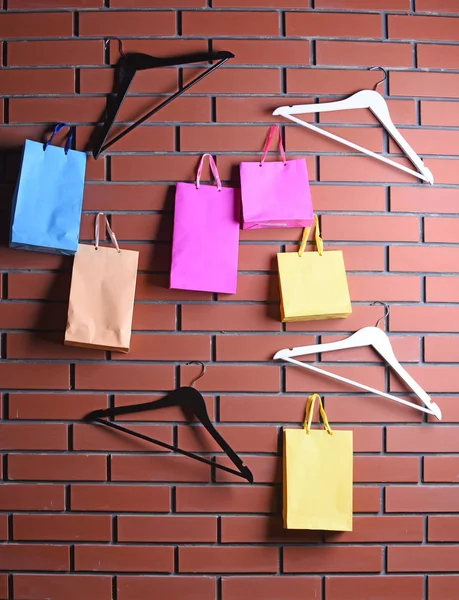 Saco de compras colorido e cabide guarda-roupa na parede de tijolo marrom — Fotografia de Stock