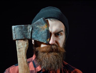 Şapkalı yakışıklı sakallı adam siyah arka planda balta tutuyor.