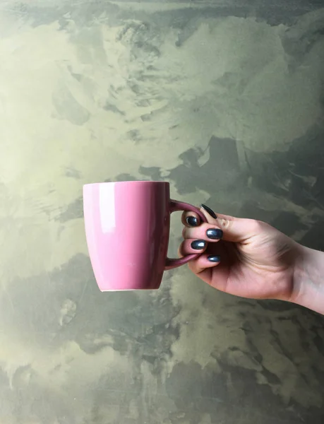 Розовый чай или чашка кофе в руке на текстурированном фоне — стоковое фото