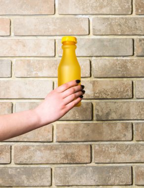 Sarı cam veya plastik şişe bej renkli arka plan üzerinde elinde