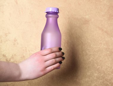 Menekşe cam veya plastik şişe bej renkli arka plan üzerinde elinde