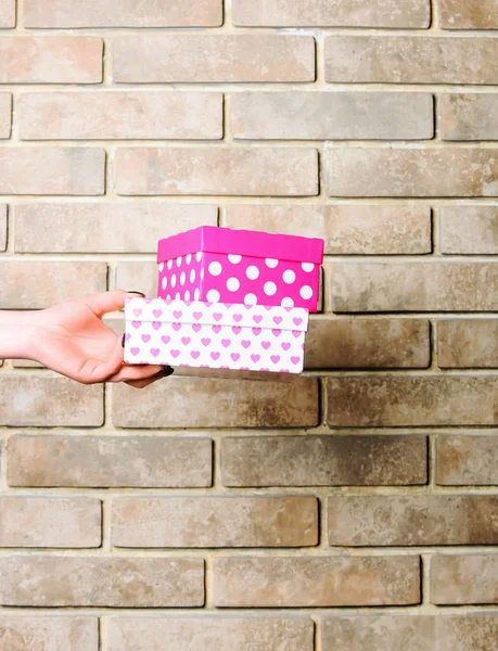 Caixa de presente manchado colorido na mão feminina na parede de tijolo — Fotografia de Stock
