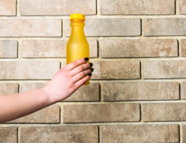 Sarı cam veya plastik şişe bej renkli arka plan üzerinde elinde