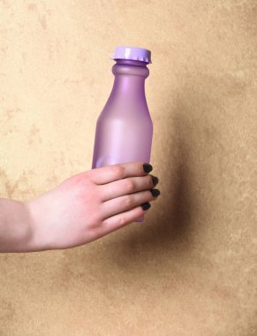 Menekşe cam veya plastik şişe bej renkli arka plan üzerinde elinde