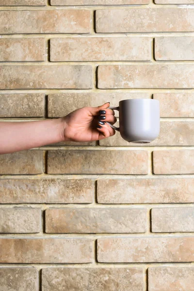 Blue tea or coffee cup in hand on brick wall — Stock Photo, Image