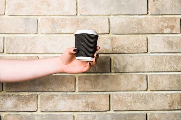 Copo de café de papel ou plástico na mão na parede de tijolo — Fotografia de Stock