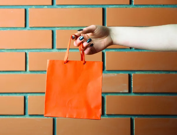 Saco de compras laranja na mão feminina na parede de tijolo — Fotografia de Stock