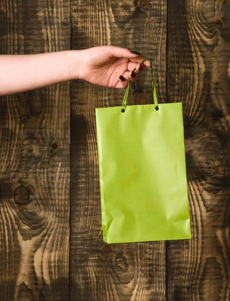 Saco de compras verde na mão feminina no fundo de madeira — Fotografia de Stock