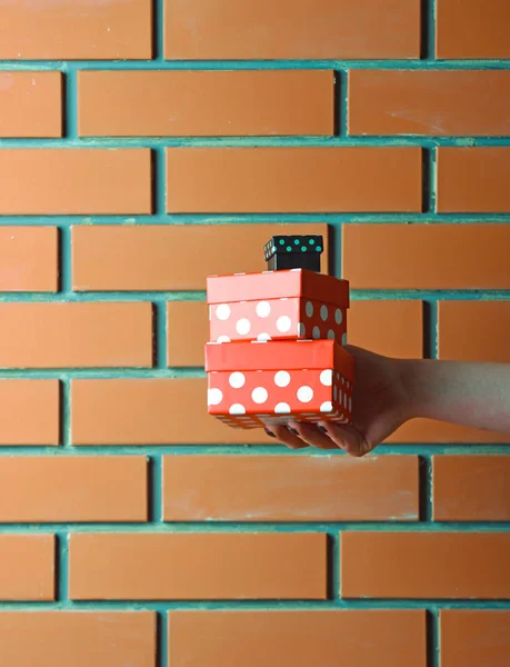 Caja de regalo manchado colorido en mano femenina en la pared de ladrillo — Foto de Stock