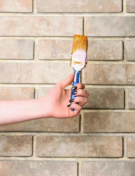 paint brush in female hand on brick wall