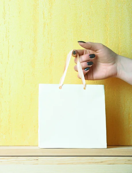 Bolsa de compras ligera en mano femenina en pared amarilla — Foto de Stock