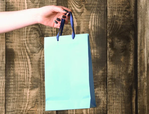 Blue shopping bag in female hand on wooden background — Stock Photo, Image