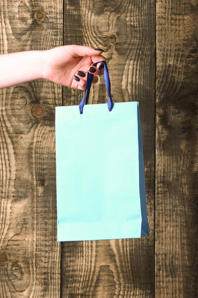 blue shopping bag in female hand on wooden background
