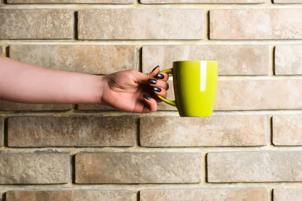 Té amarillo o taza de café en la mano en la pared de ladrillo — Foto de Stock