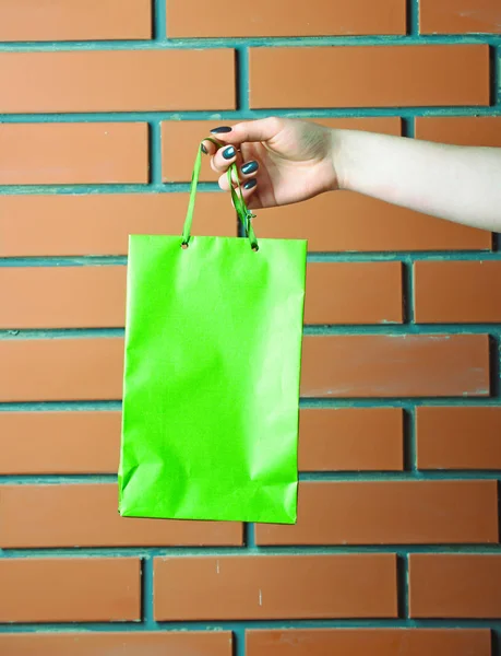 벽돌 벽에 여성 손에 녹색 쇼핑 가방 — 스톡 사진