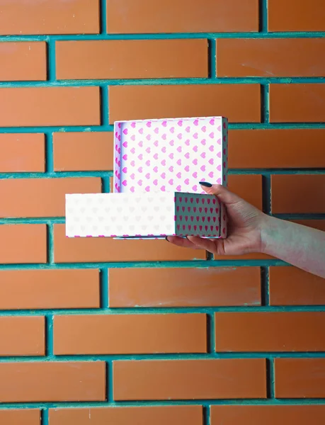 Caixa de presente manchado colorido na mão feminina na parede de tijolo — Fotografia de Stock