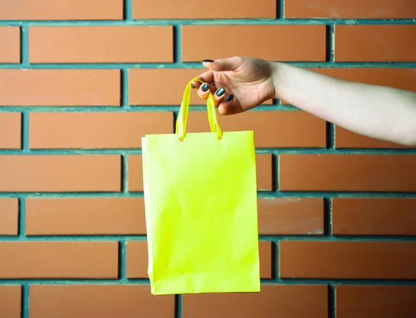 벽돌 벽에 여성 손에 녹색 쇼핑 가방 — 스톡 사진
