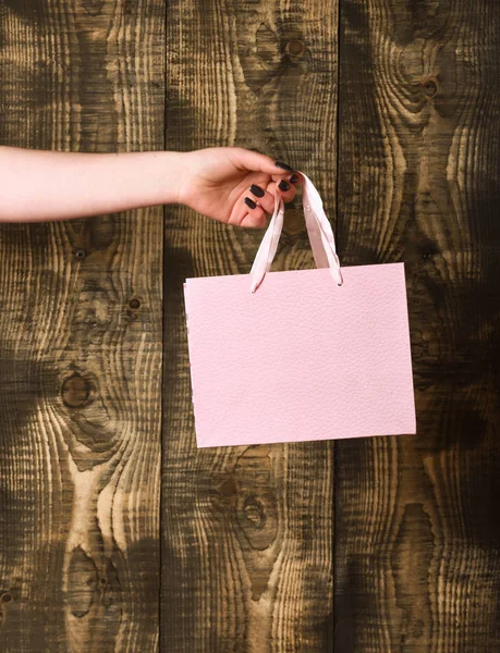 Saco de compras rosa na mão feminina no fundo de madeira — Fotografia de Stock