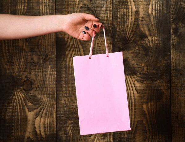 pink shopping bag in female hand on wooden background