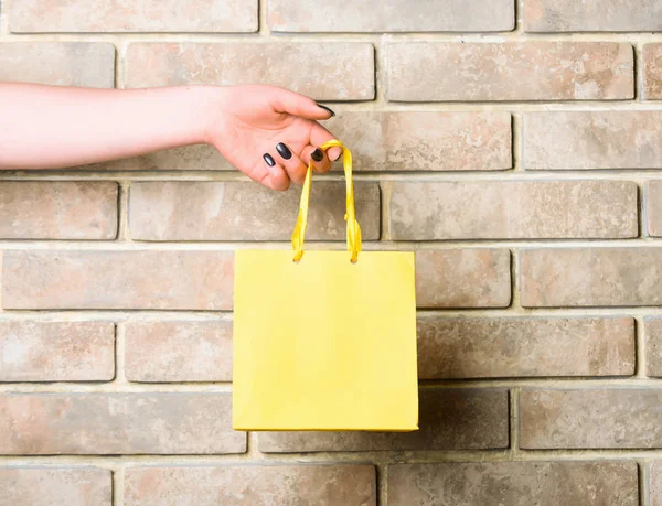 Saco de compras amarelo na mão feminina na parede de tijolo — Fotografia de Stock