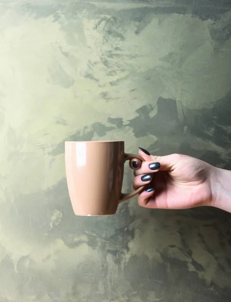beige tea or coffee cup in hand on textured background