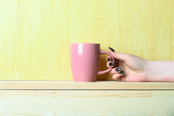 pink tea or coffee cup in hand on yellow background