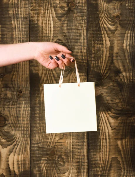 Saco de compras branco na mão feminina no fundo de madeira — Fotografia de Stock